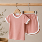 Pink children's outfit with white trim on hangers against a beige background